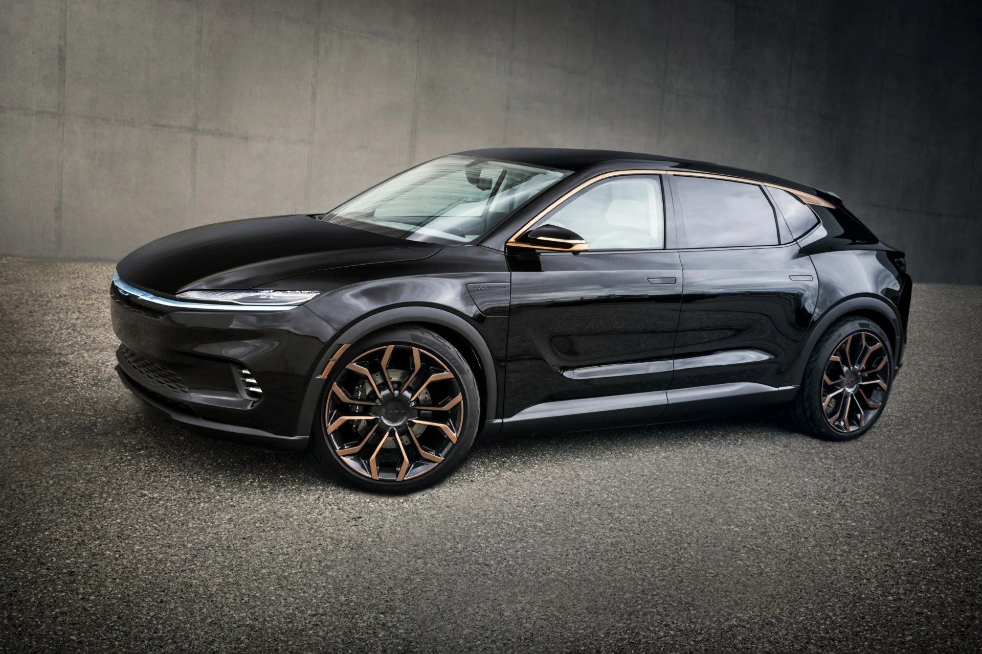 Glossy black electric SUV with bronze-accented wheels and trim parked on asphalt against a concrete wall.