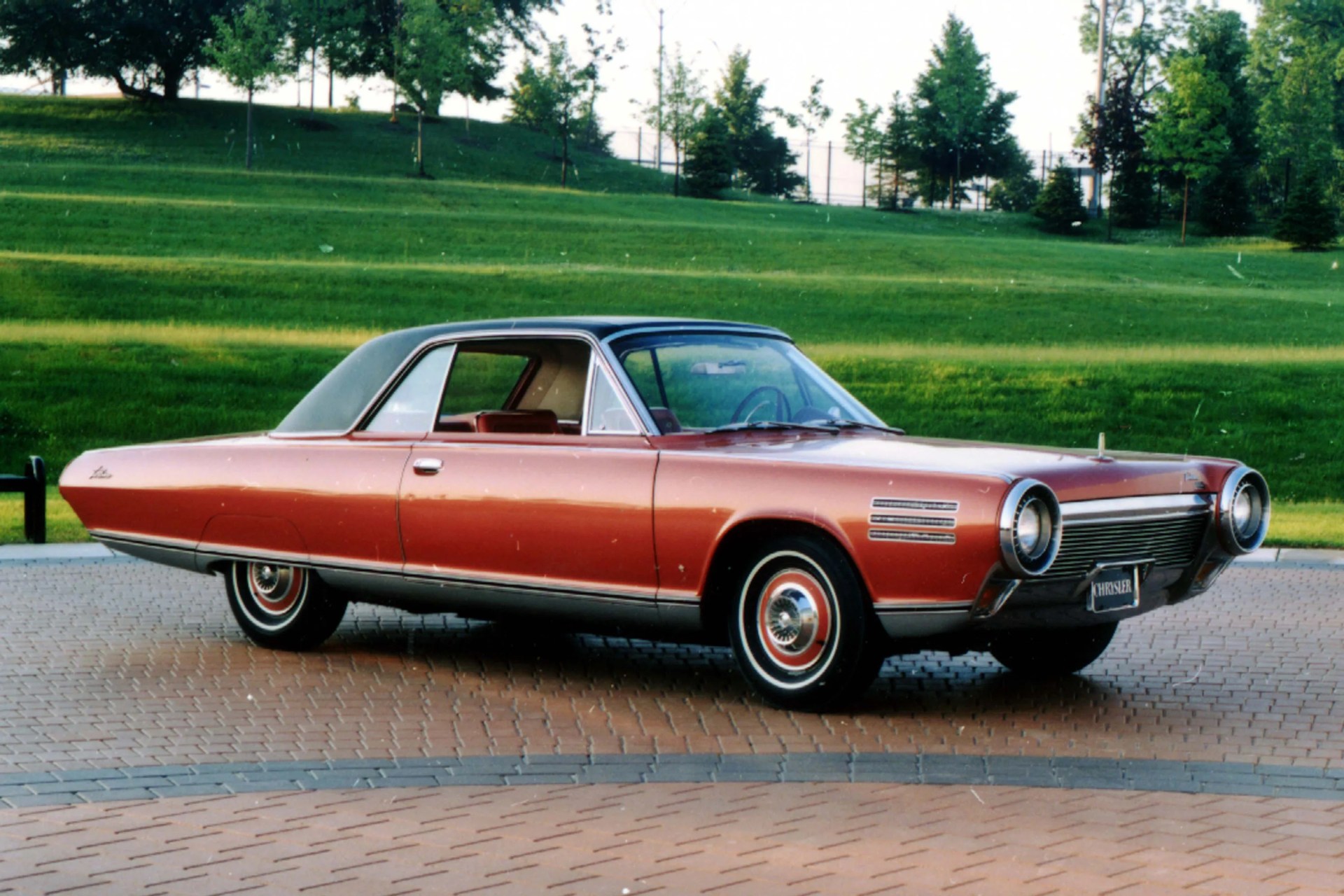 Copper-colored vintage Chrysler car with a black vinyl roof parked on a brick driveway with green grass in the background.