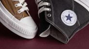 Close-up of brown and black Converse All Star sneakers with white laces and rubber soles on a dark surface.