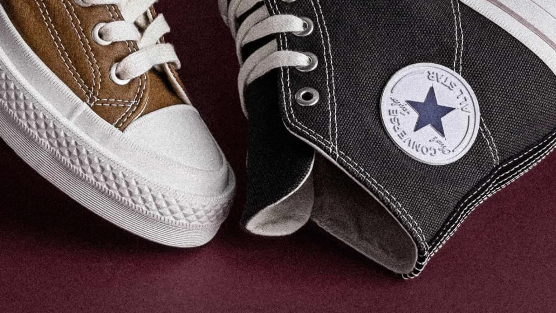 Close-up of brown and black Converse All Star sneakers with white laces and rubber soles on a dark surface.