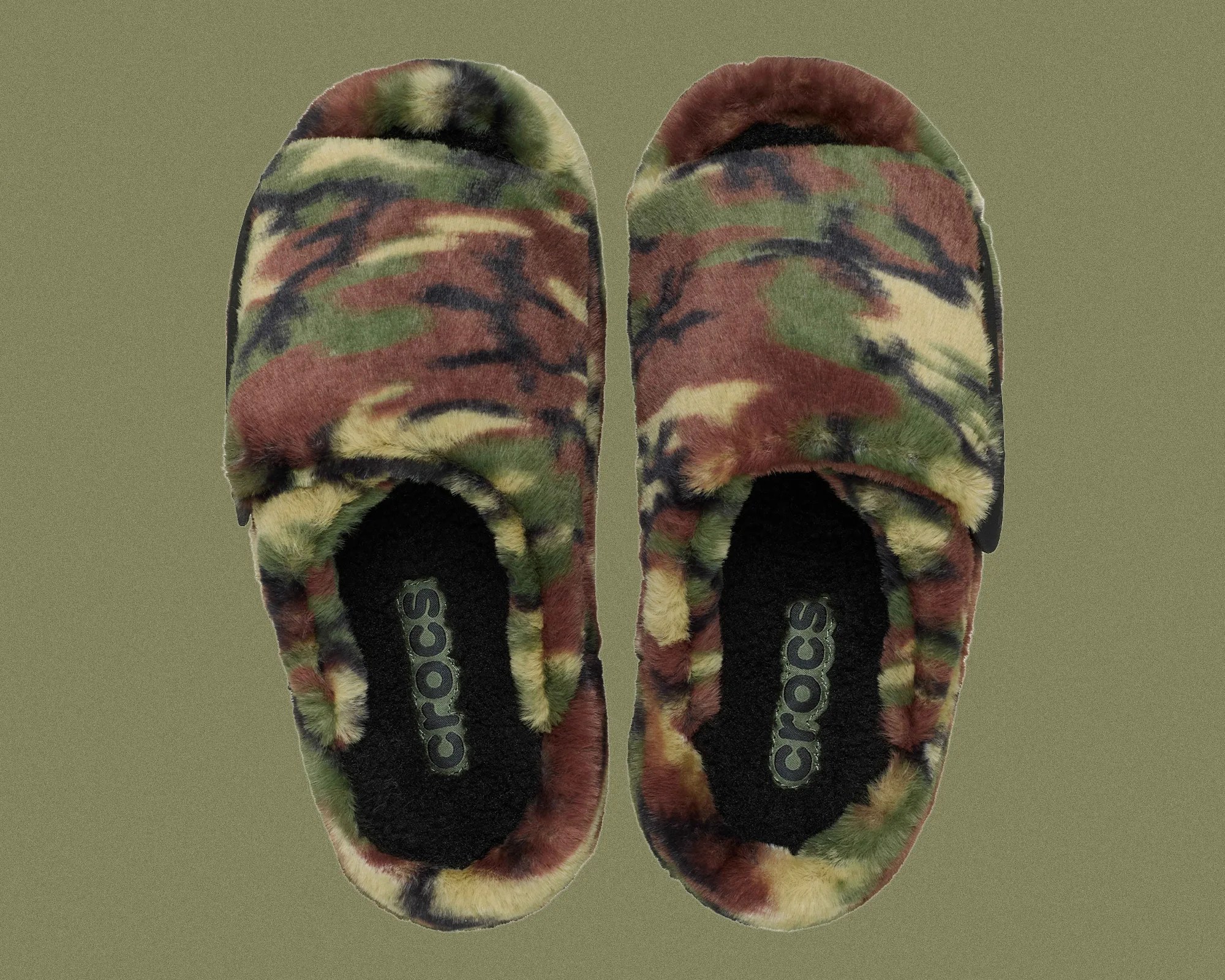 Pair of fuzzy Crocs slippers with green, brown, and black camouflage pattern on a green background.