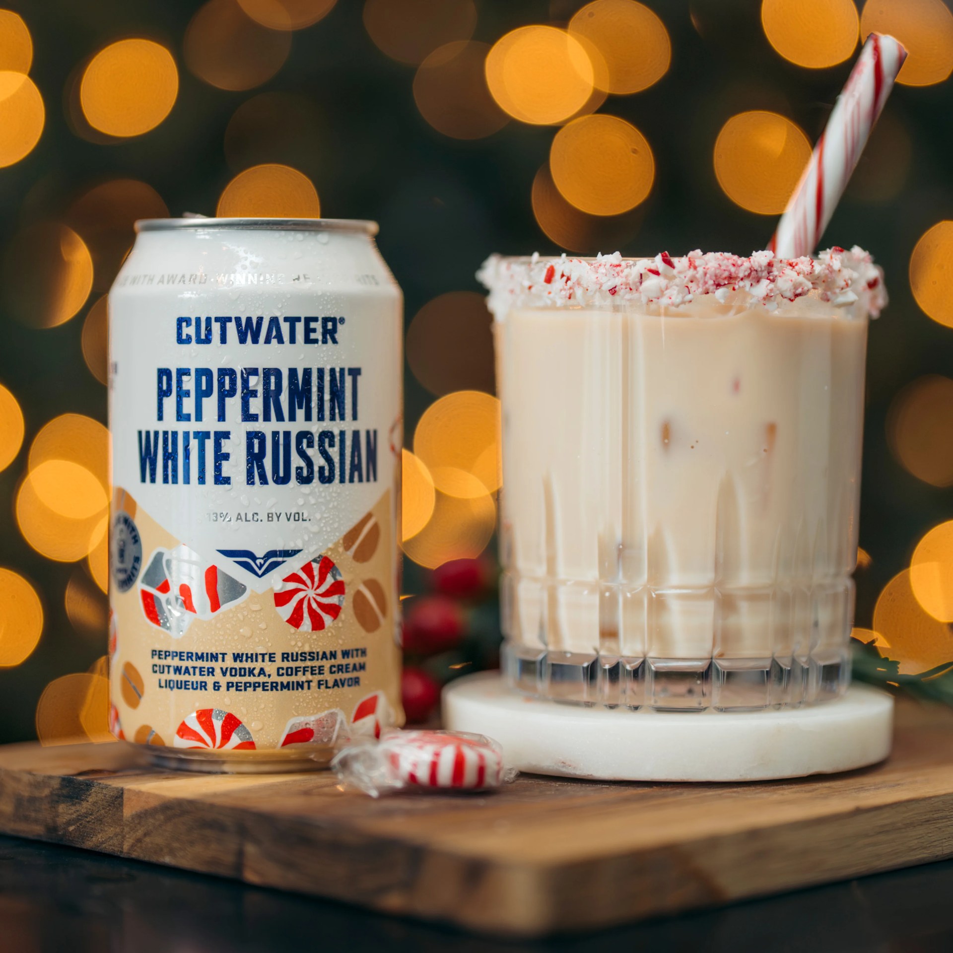 Can of Cutwater Peppermint White Russian next to a glass with a creamy drink, crushed peppermint rim, and a peppermint stick.