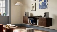 Dark wood floating media console with vinyl records, stereo receiver, turntable, and two gray speakers in a living room corner.