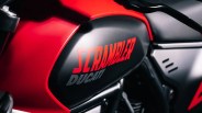 Black motorcycle fuel tank with red "SCRAMBLER" and gray "DUCATI" logos on a red bike frame.