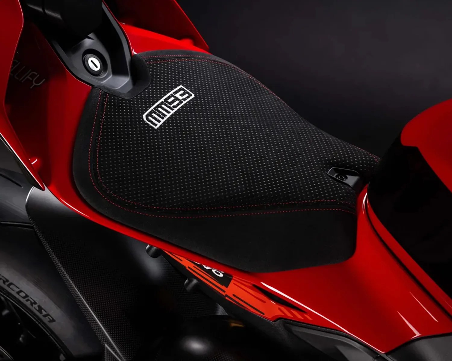 Black textured motorcycle seat with red stitching and white "MUSE" logo on a red bike frame.