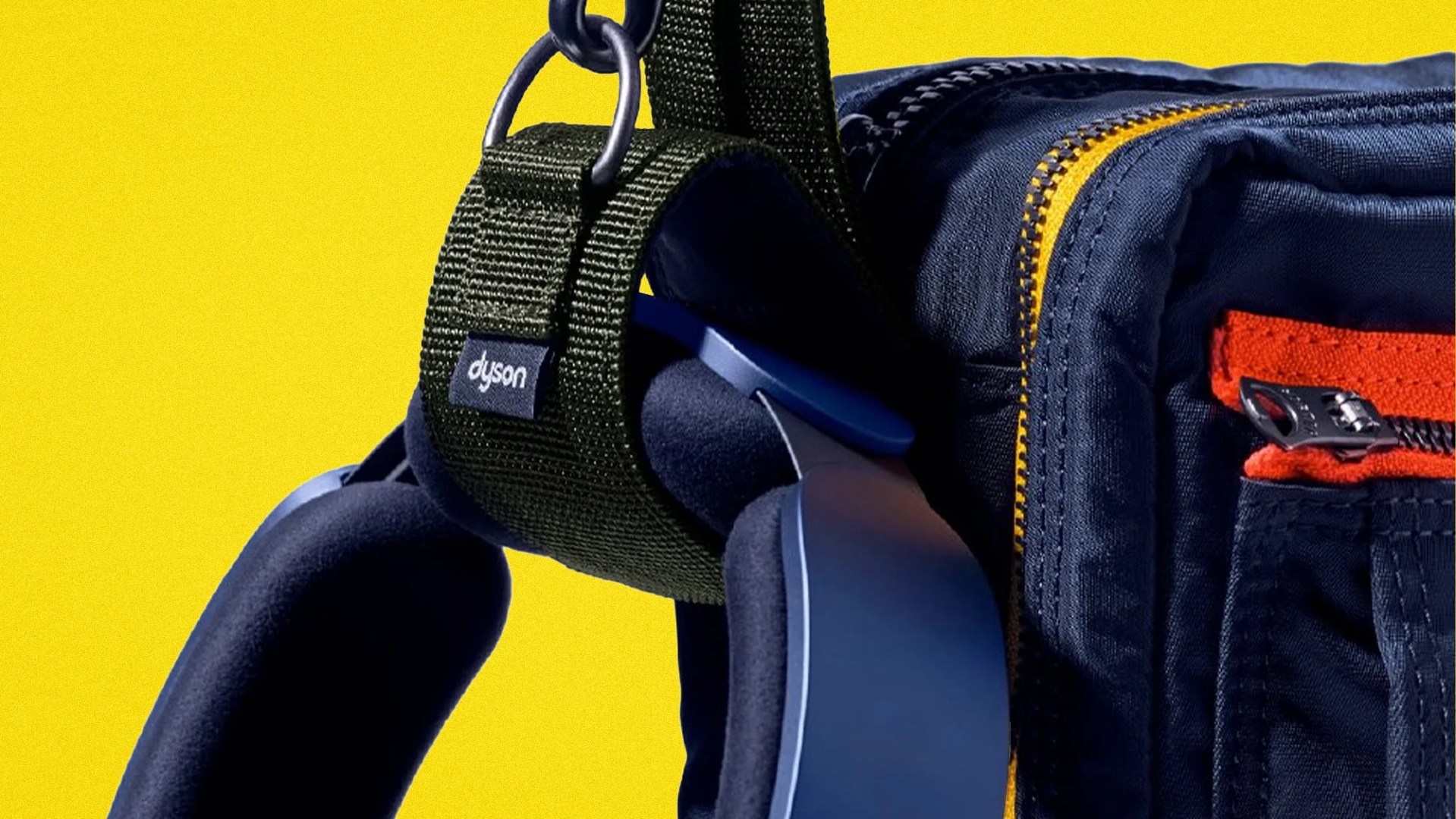 Close-up of a navy blue and black Dyson strap attached to a navy bag with yellow and red zipper details against a yellow background.