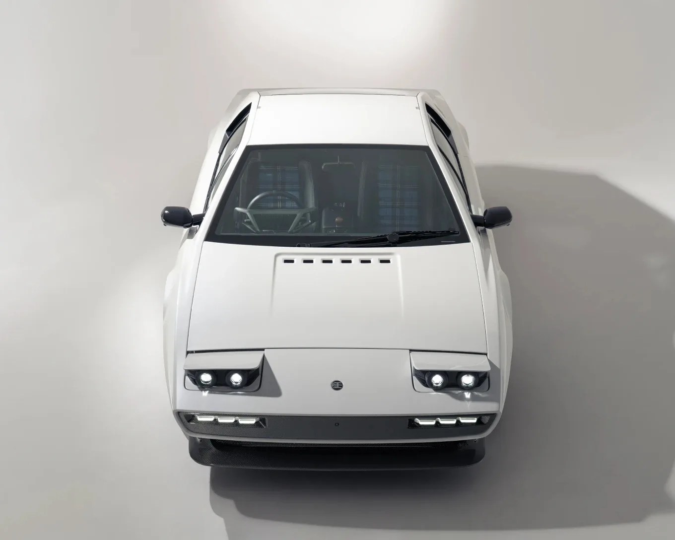 White vintage sports car with pop-up headlights and plaid interior seats, viewed from the front.