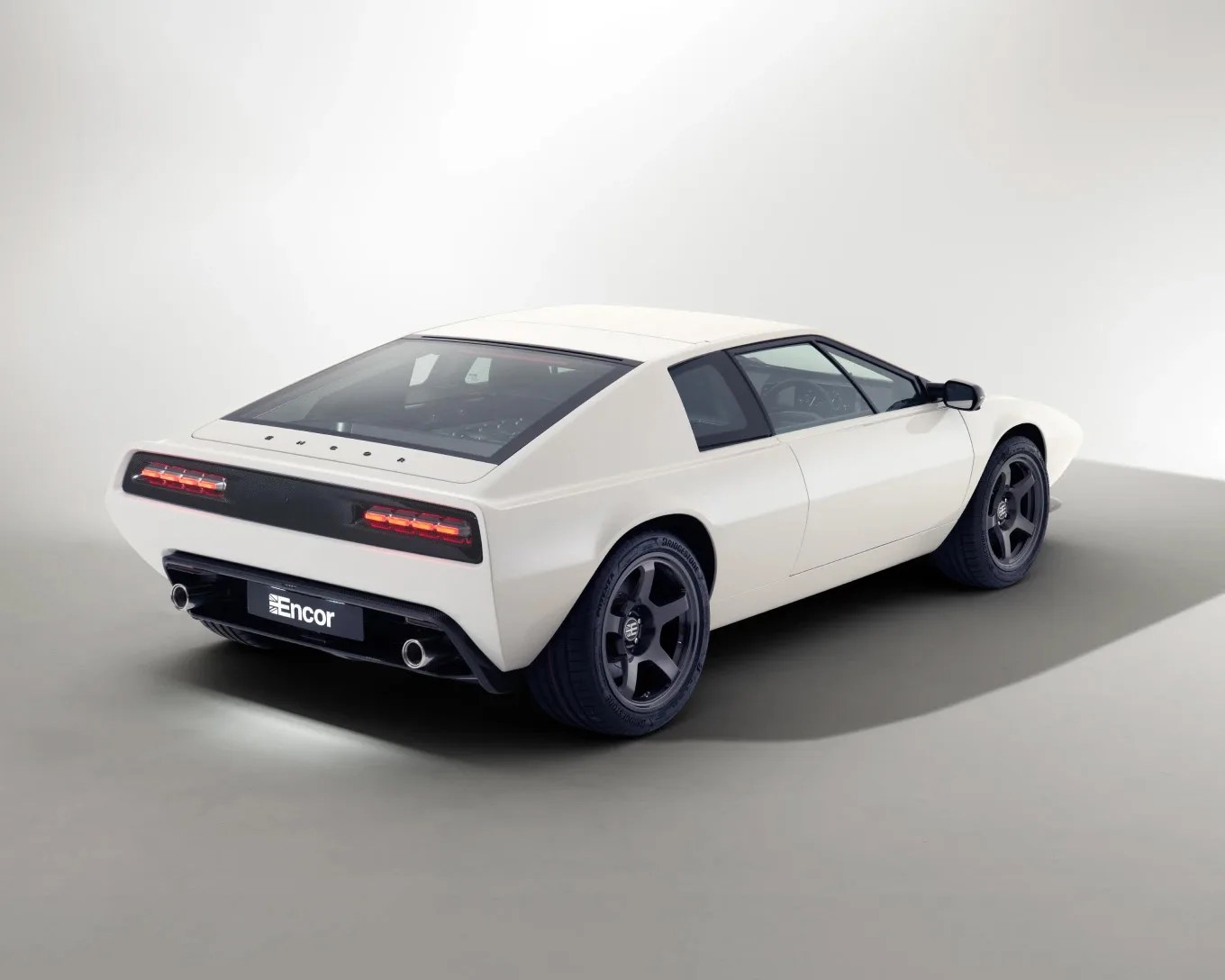 White retro-style sports car with black wheels and rear taillights in a studio setting.