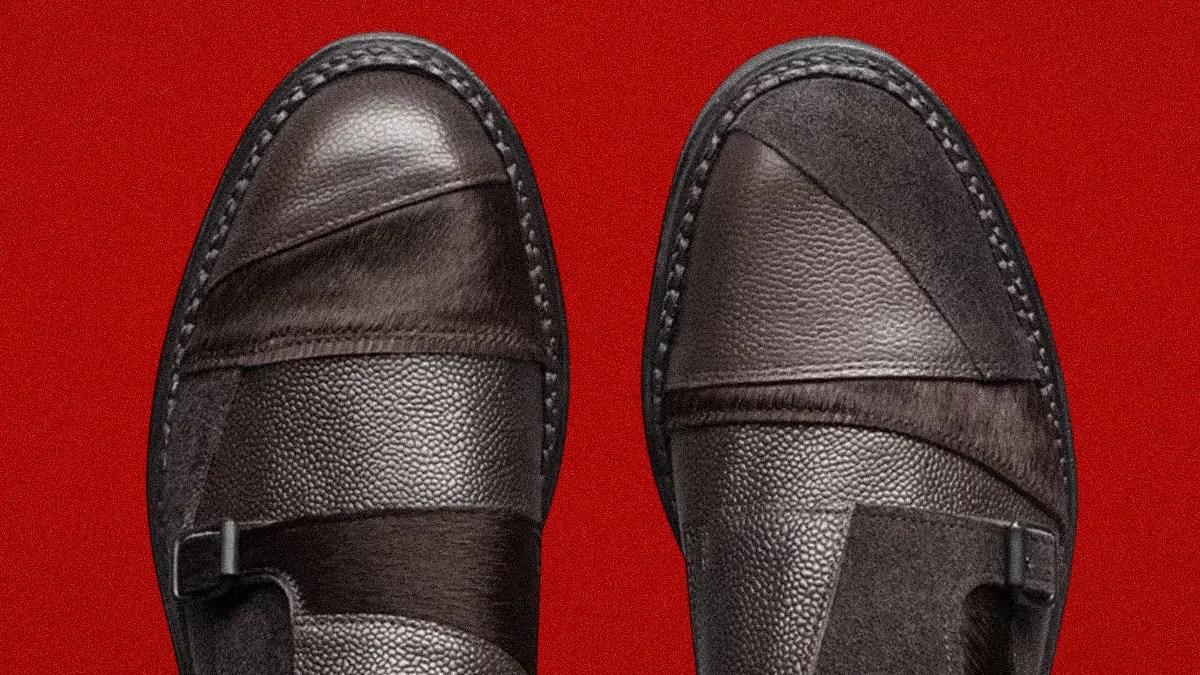 Pair of dark brown leather shoes with textured and smooth panels on a red background.