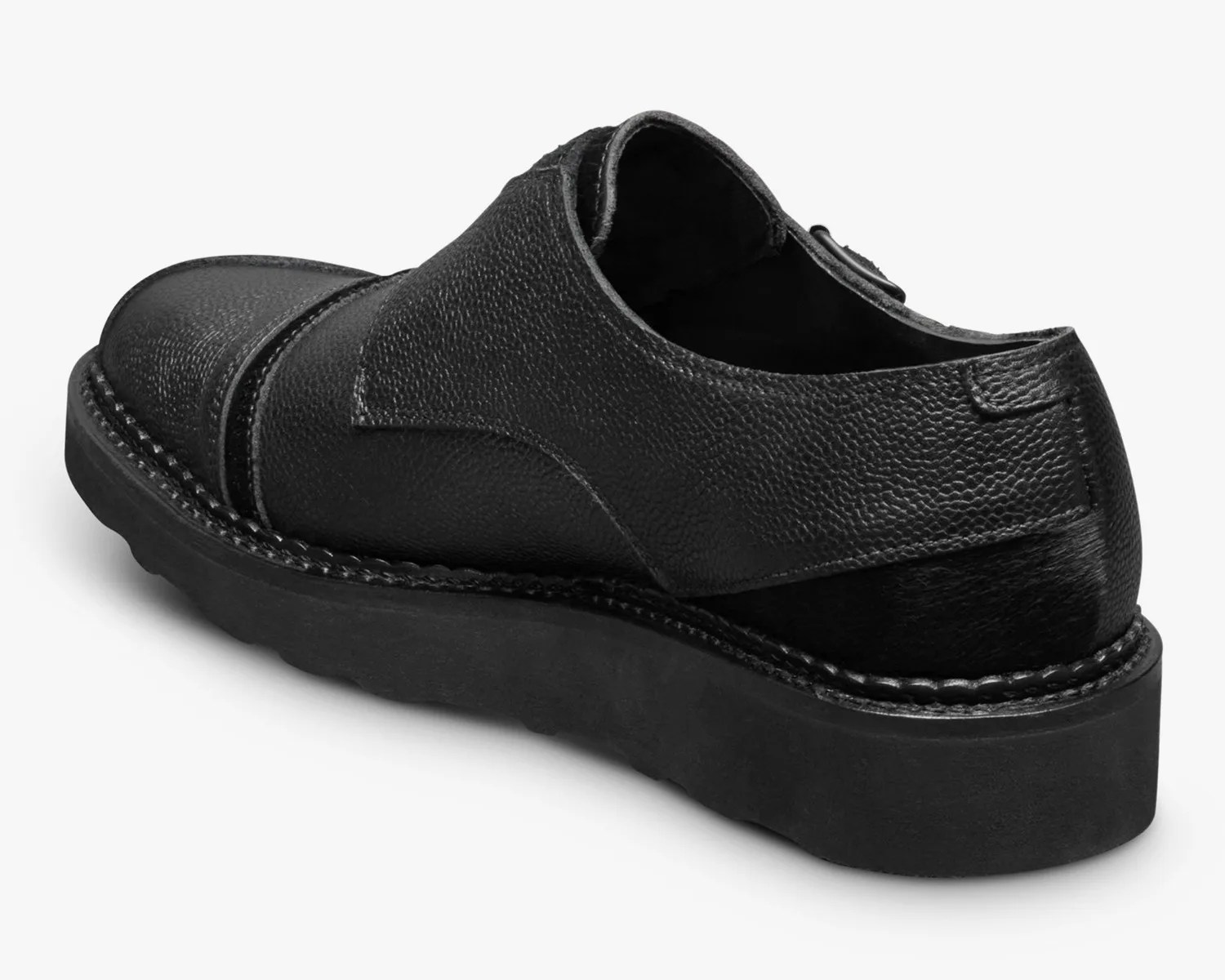 Black textured leather slip-on shoe with thick black sole viewed from the back side.