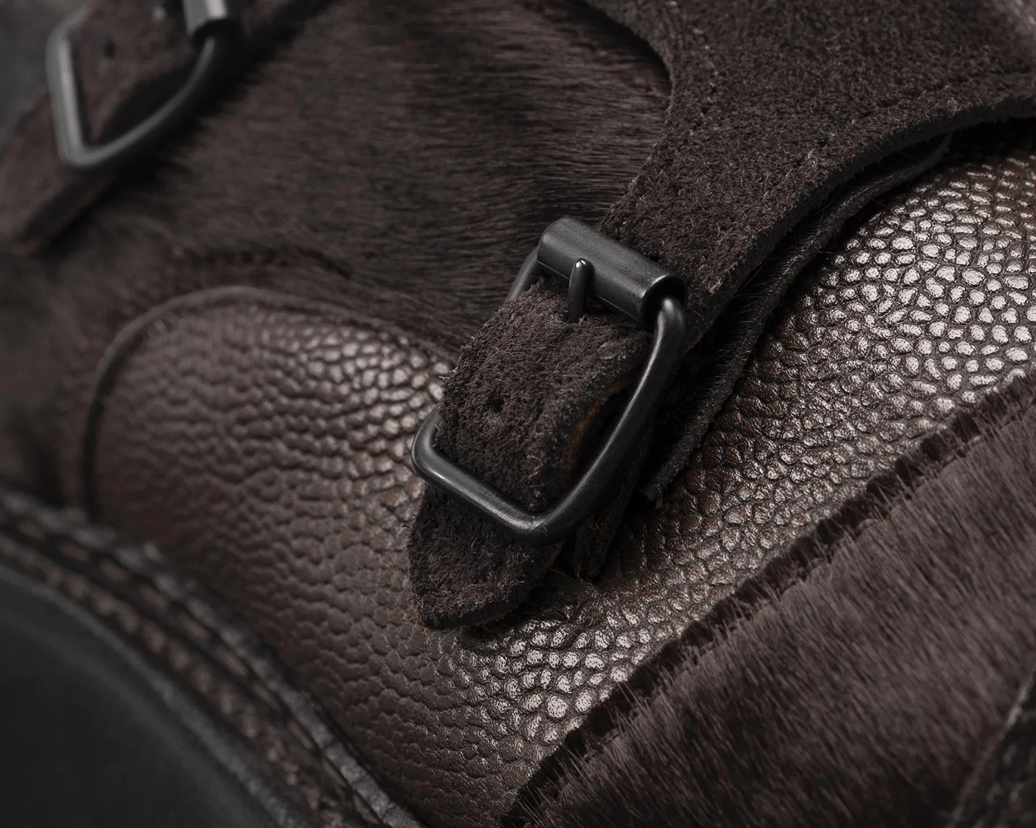 Close-up of dark brown textured leather and suede with a black metal buckle.
