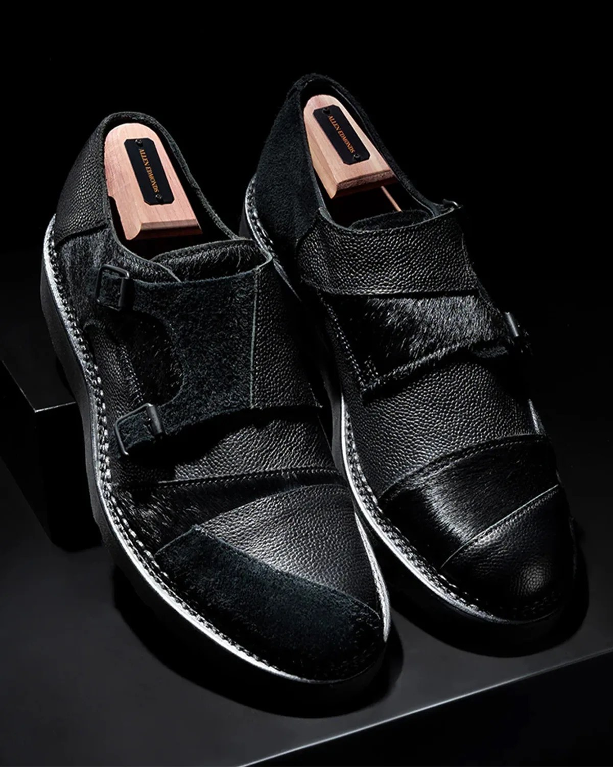 Pair of black textured leather and suede monk strap shoes with wooden shoe trees inside.