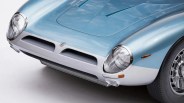 Front corner of a light blue and white vintage car showing round headlights, grille, and detailed wheel.
