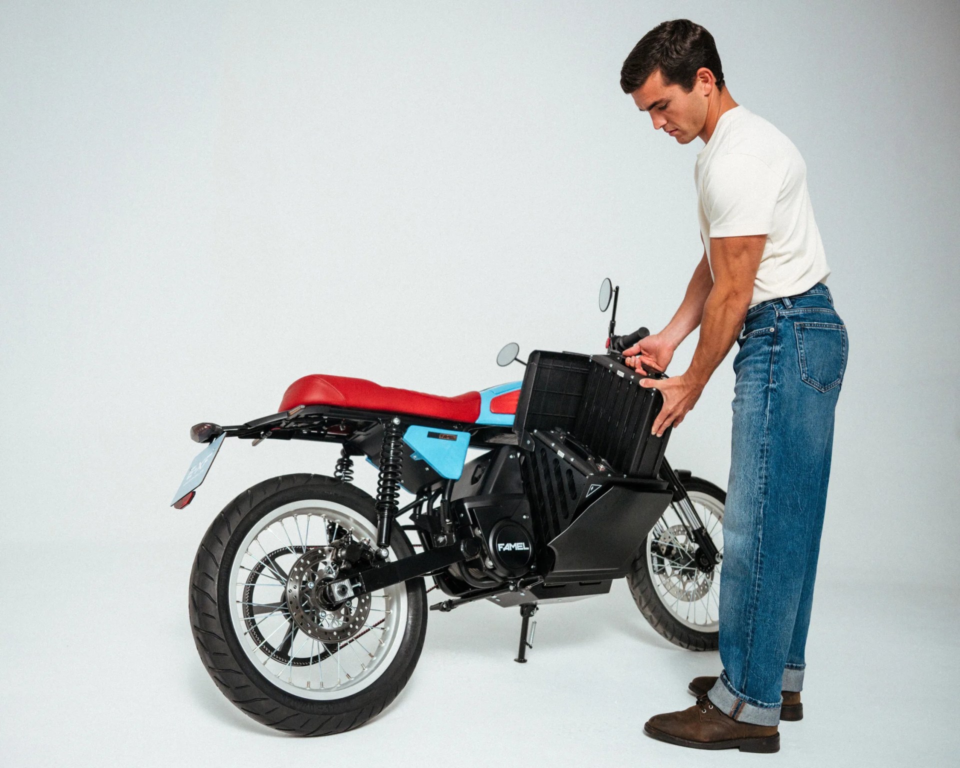 Man in white t-shirt and jeans placing a black storage box into a blue and red Famel electric motorcycle.