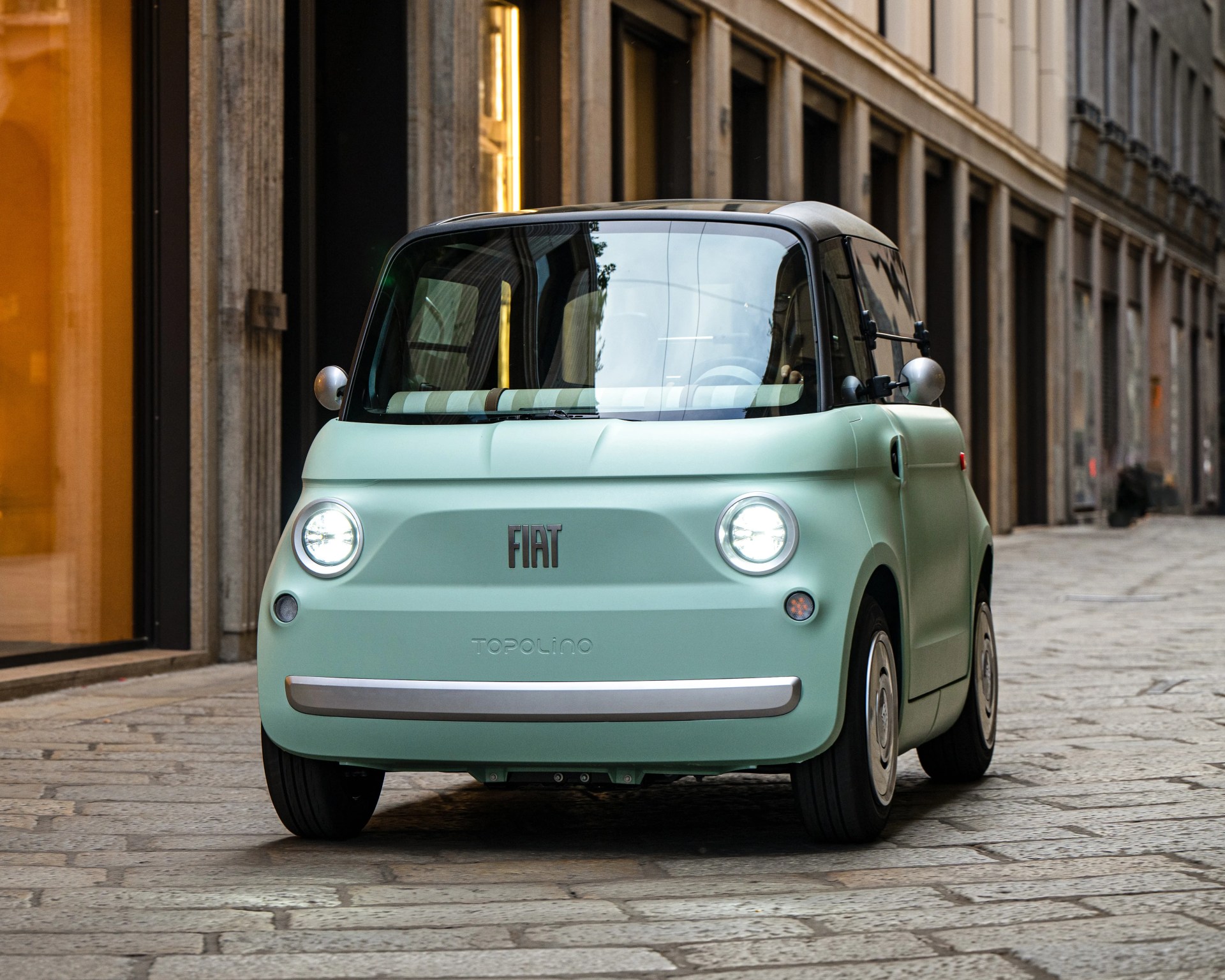 Mint green Fiat Topolino electric car with round headlights on a cobblestone street.