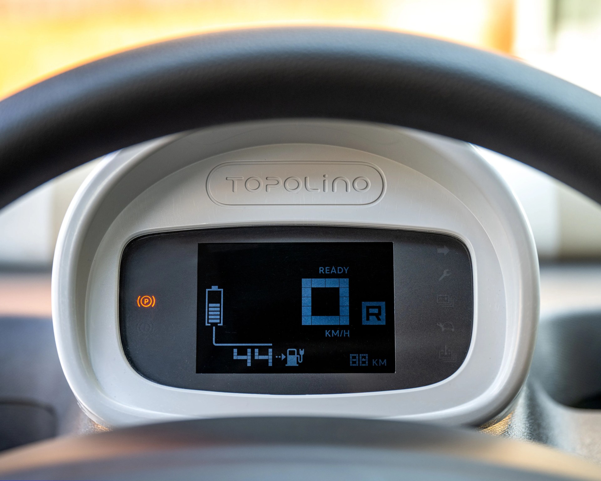 Digital dashboard display of a Topolino vehicle showing battery level, speed, and reverse gear indicator.