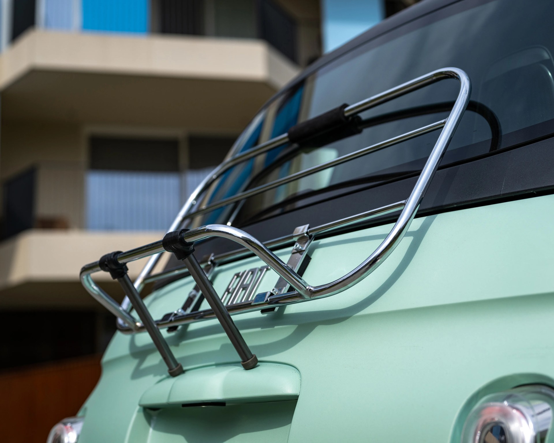 Chrome luggage rack mounted on the rear of a light green vintage car.
