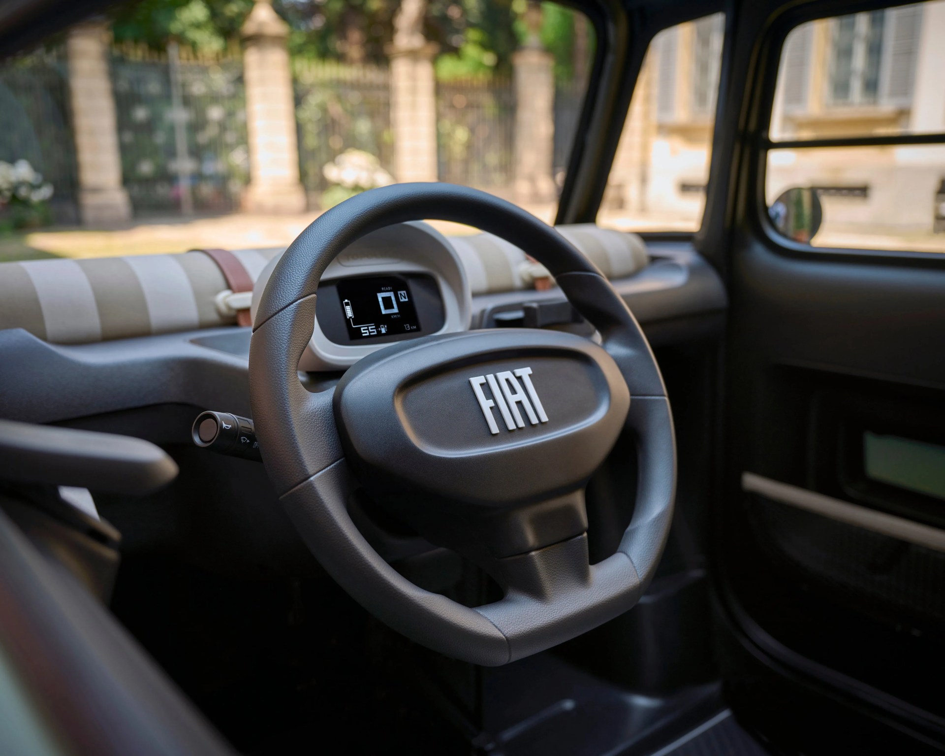 Black Fiat steering wheel with digital dashboard and beige striped fabric dashboard in a car interior.