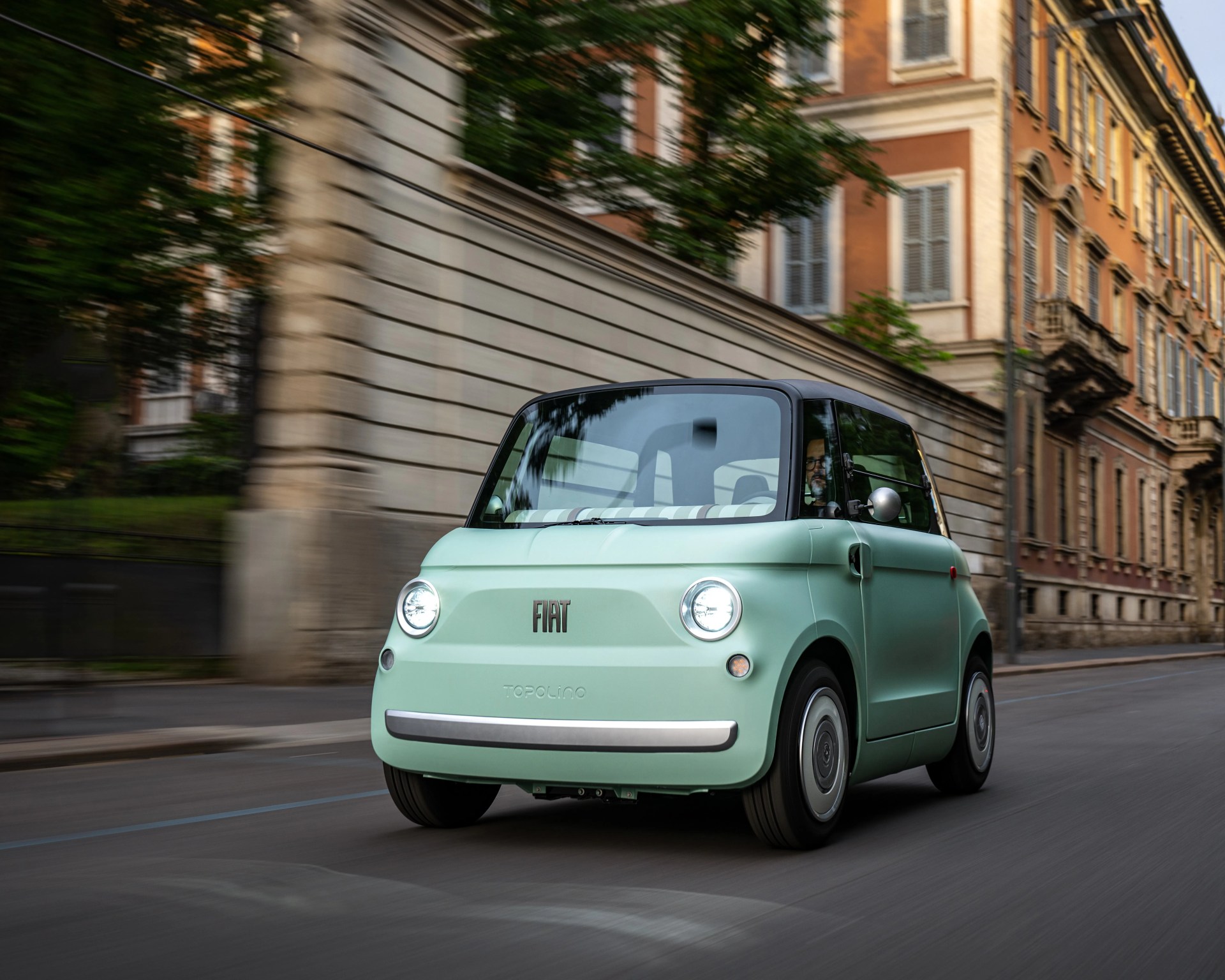 Mint green Fiat Topolino compact car with round headlights driving on a city street.