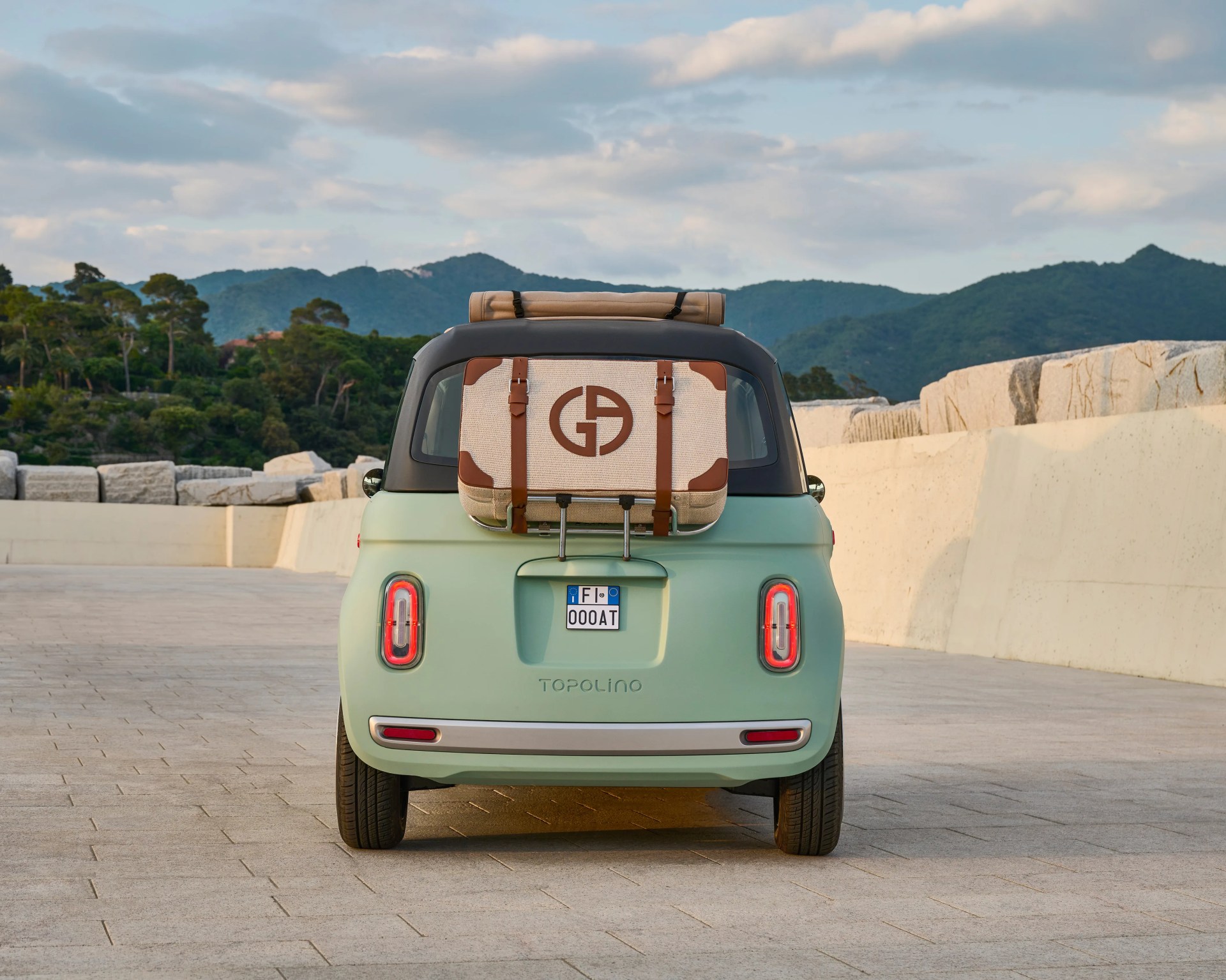 Rear view of a mint green Fiat Topolino with a beige and brown luggage bag attached to the back.