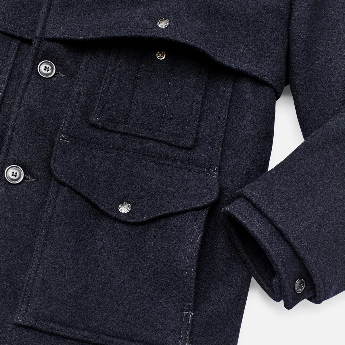 Close-up of a dark navy wool jacket showing buttoned flap pockets and a buttoned cuff.