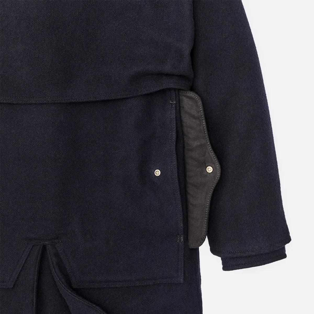 Close-up of a navy blue wool coat sleeve and pocket with a snap button flap.