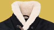 Black coat with large buttons and a thick cream-colored shearling collar against a yellow background.
