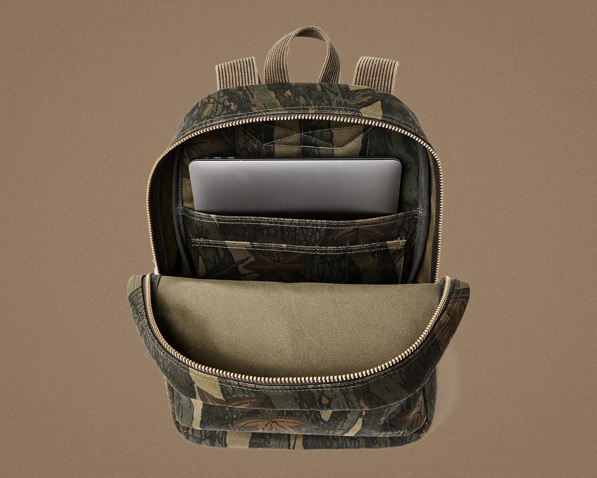 Camouflage-patterned backpack with a laptop partially inserted in the internal sleeve, shown open against a brown background.