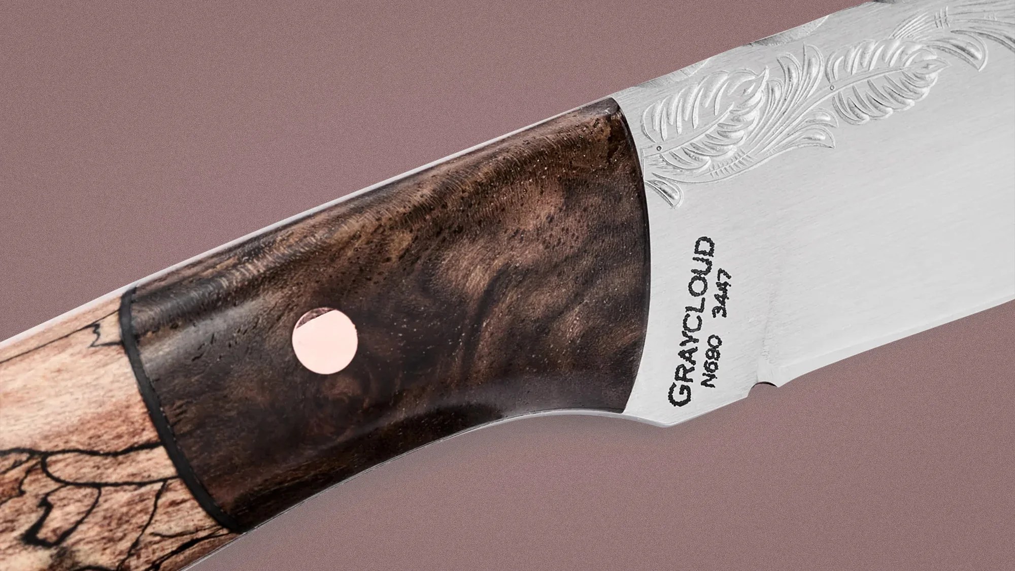 Close-up of a knife handle made of dark and light wood with a metal rivet and engraved blade reading "GRAYCLOUD N690 3447.