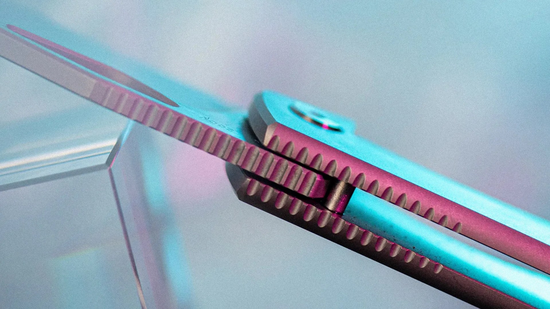 Close-up of a metallic folding knife hinge with textured grip and blue-pink lighting.