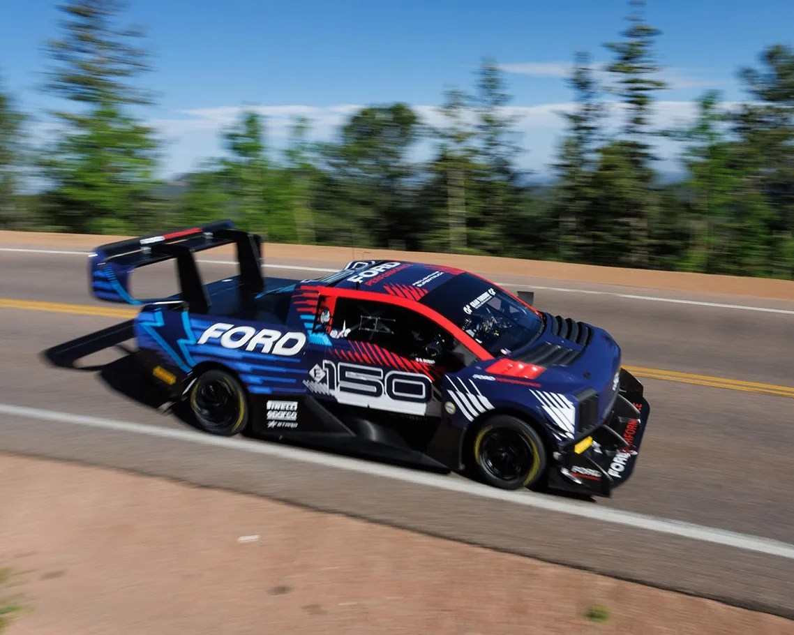 Blue and red Ford race truck with number 150 speeding on a mountain road.