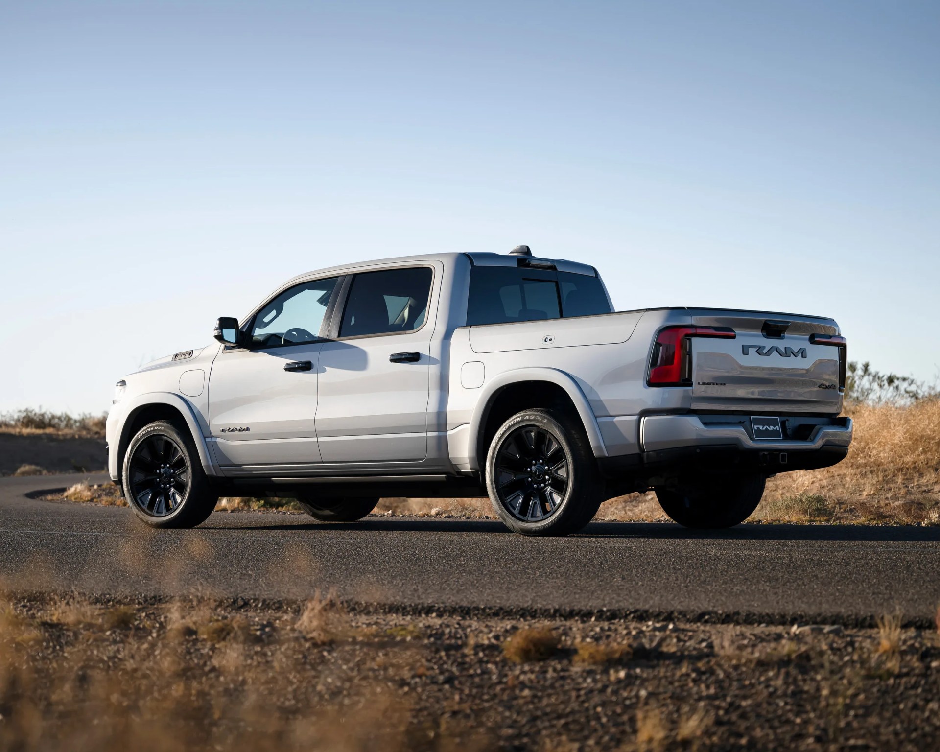 Silver RAM pickup truck with black wheels parked on a paved road in a dry grassy area.