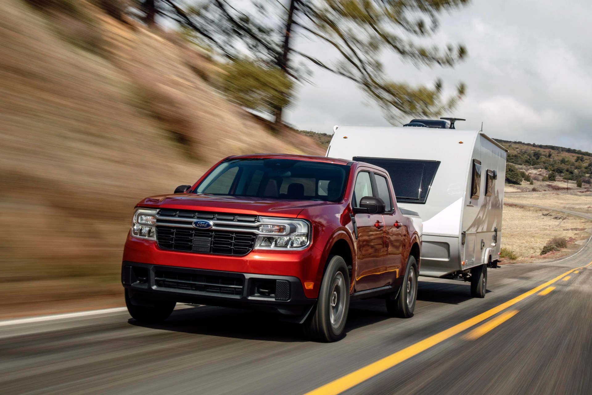 Red Ford pickup truck towing a white travel trailer on a highway with blurred background.