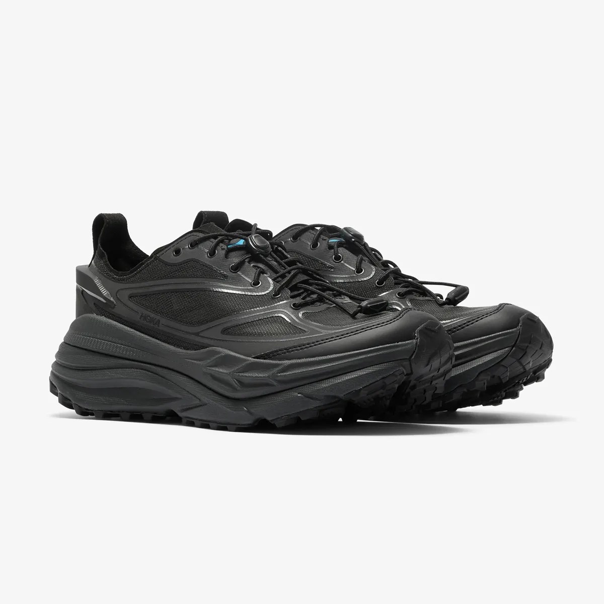 Pair of black Hoka trail running shoes with thick soles and toggle laces on a white background.
