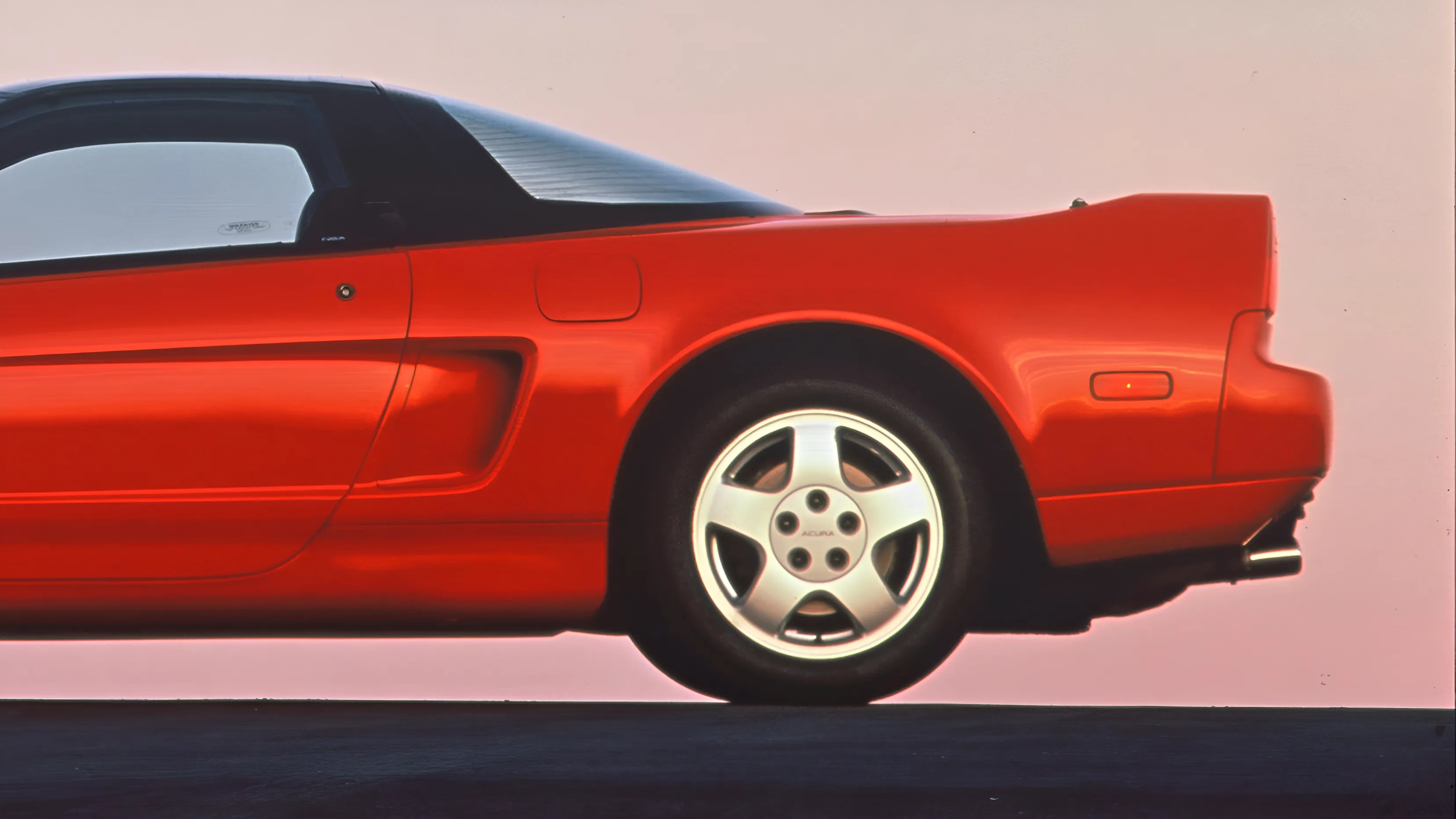 Red sports car rear side with black roof and silver five-spoke wheel on a dark surface.
