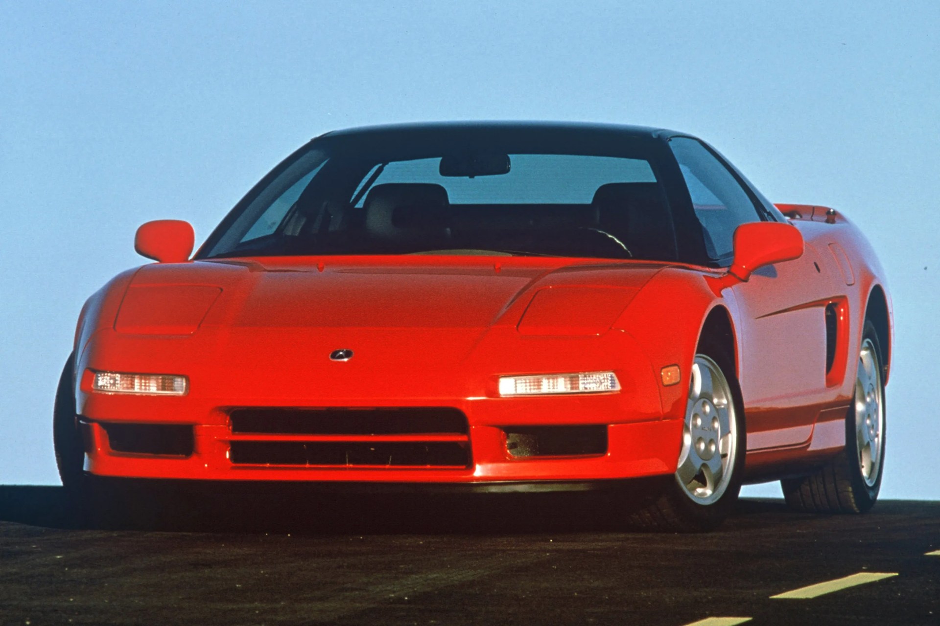 Red Acura NSX sports car front view on a road with clear blue sky background.