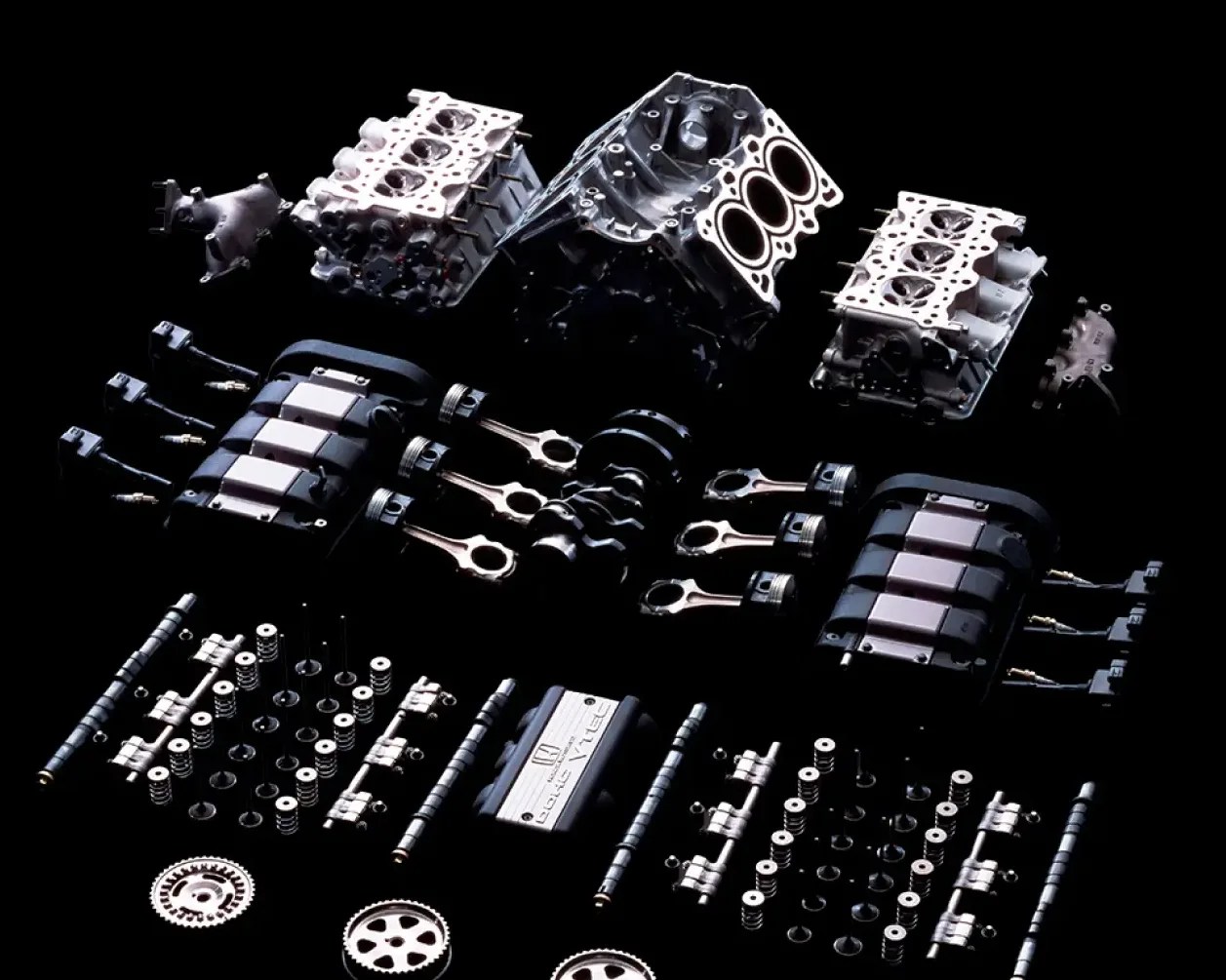 Disassembled V12 engine components including cylinder heads, pistons, crankshaft, camshafts, and valve springs arranged on a black background.
