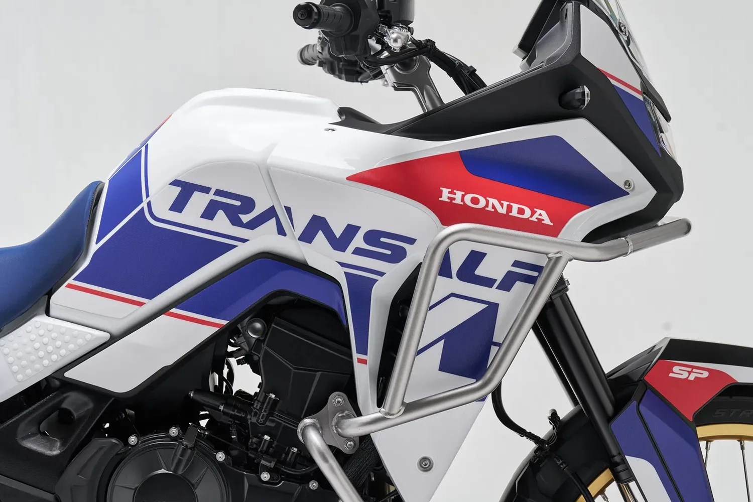 Close-up of a white, blue, and red Honda Transalp motorcycle with a silver crash bar and blue seat.