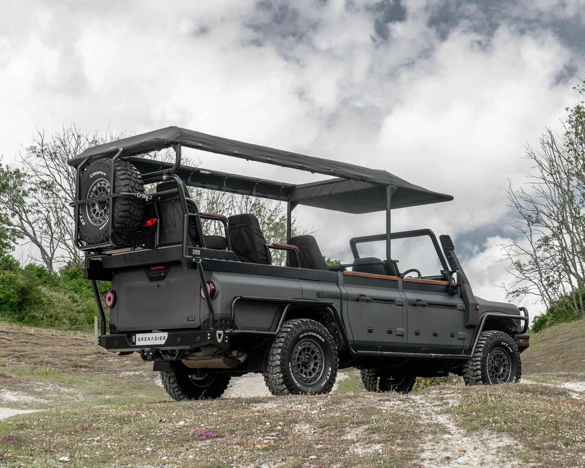 Matte black open-top off-road vehicle with rugged tires and a canopy roof parked on grassy terrain.