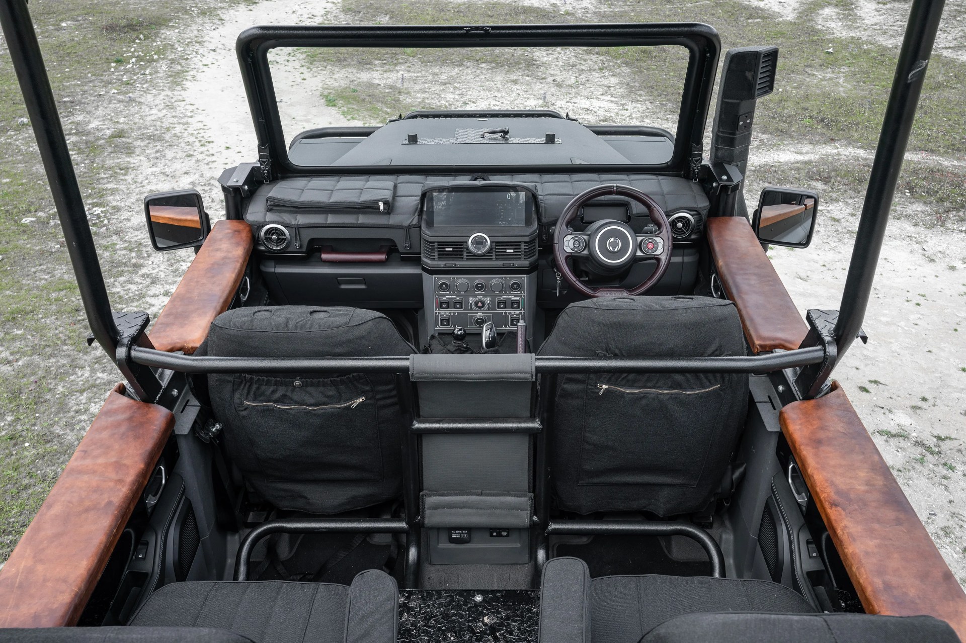 Open-top vehicle interior with black fabric seats, brown leather armrests, and a central dashboard featuring a touchscreen and multiple controls.