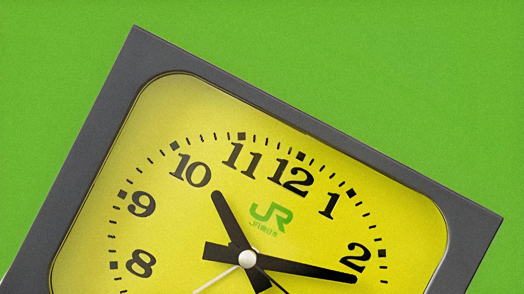 Yellow square clock with black numbers and hands showing 10:12, set against a green background.