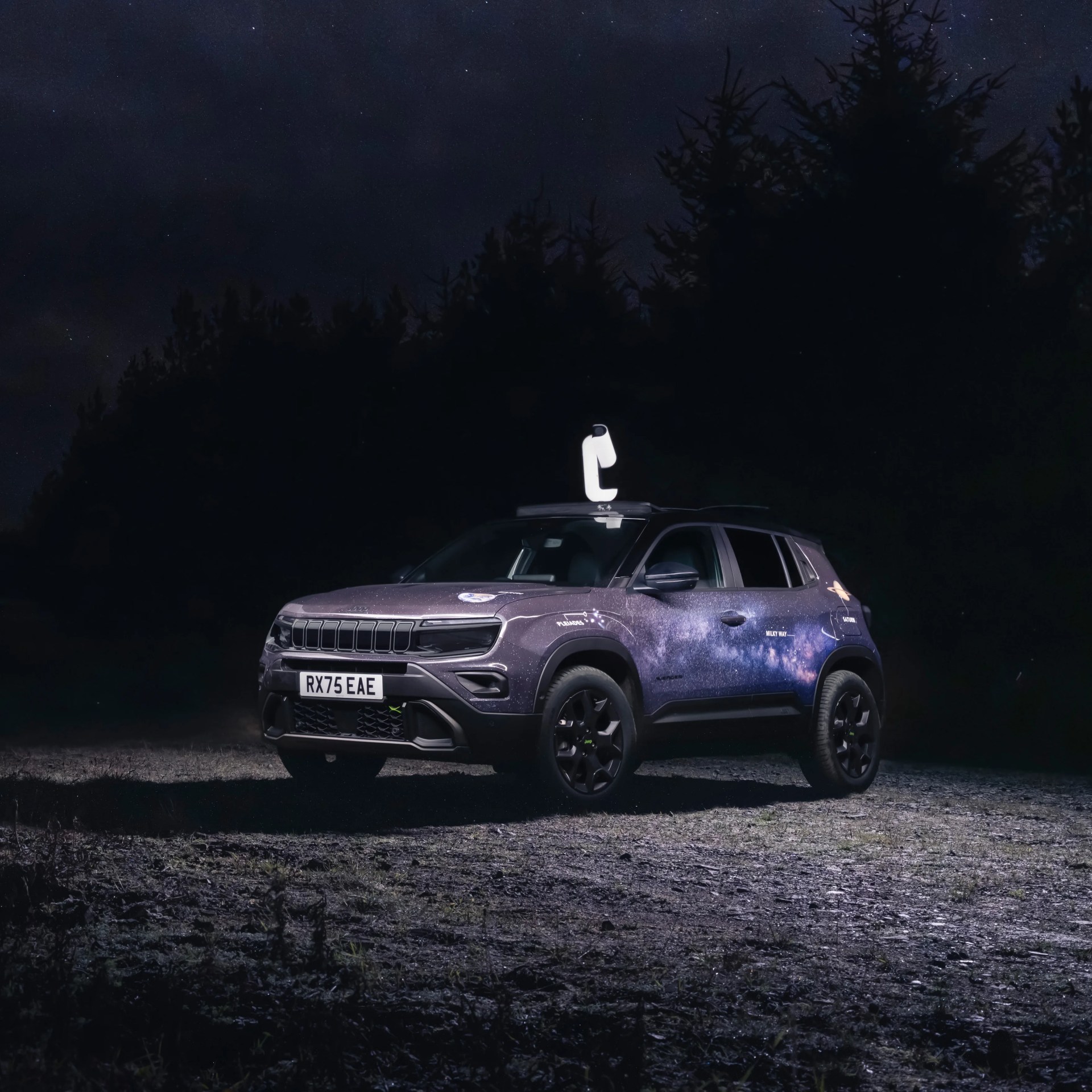 Purple SUV with galaxy-themed wrap and a white device mounted on the roof, parked on a gravel surface at night.