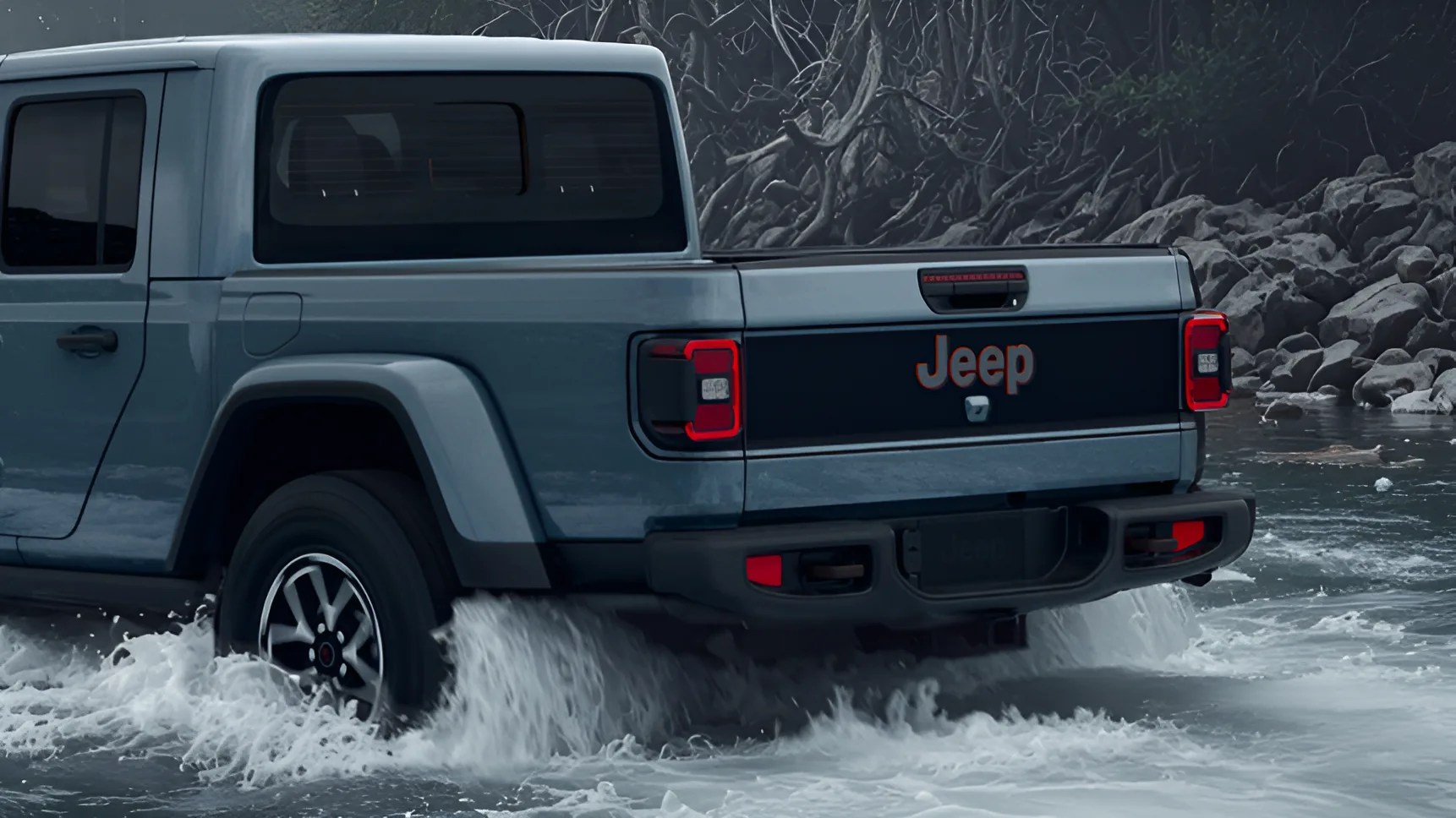 Rear side of a blue Jeep pickup truck driving through shallow water with rocky shore in the background.