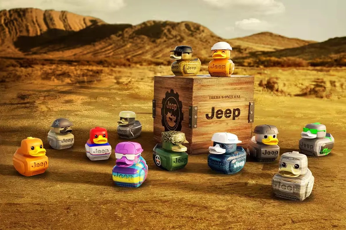 Twelve Jeep-branded rubber ducks in various colors and designs arranged around a wooden Jeep crate in a desert landscape.