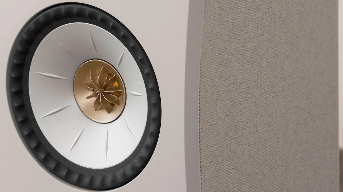 Close-up of a white speaker cone with a gold-colored central tweeter and a gray fabric speaker grille.