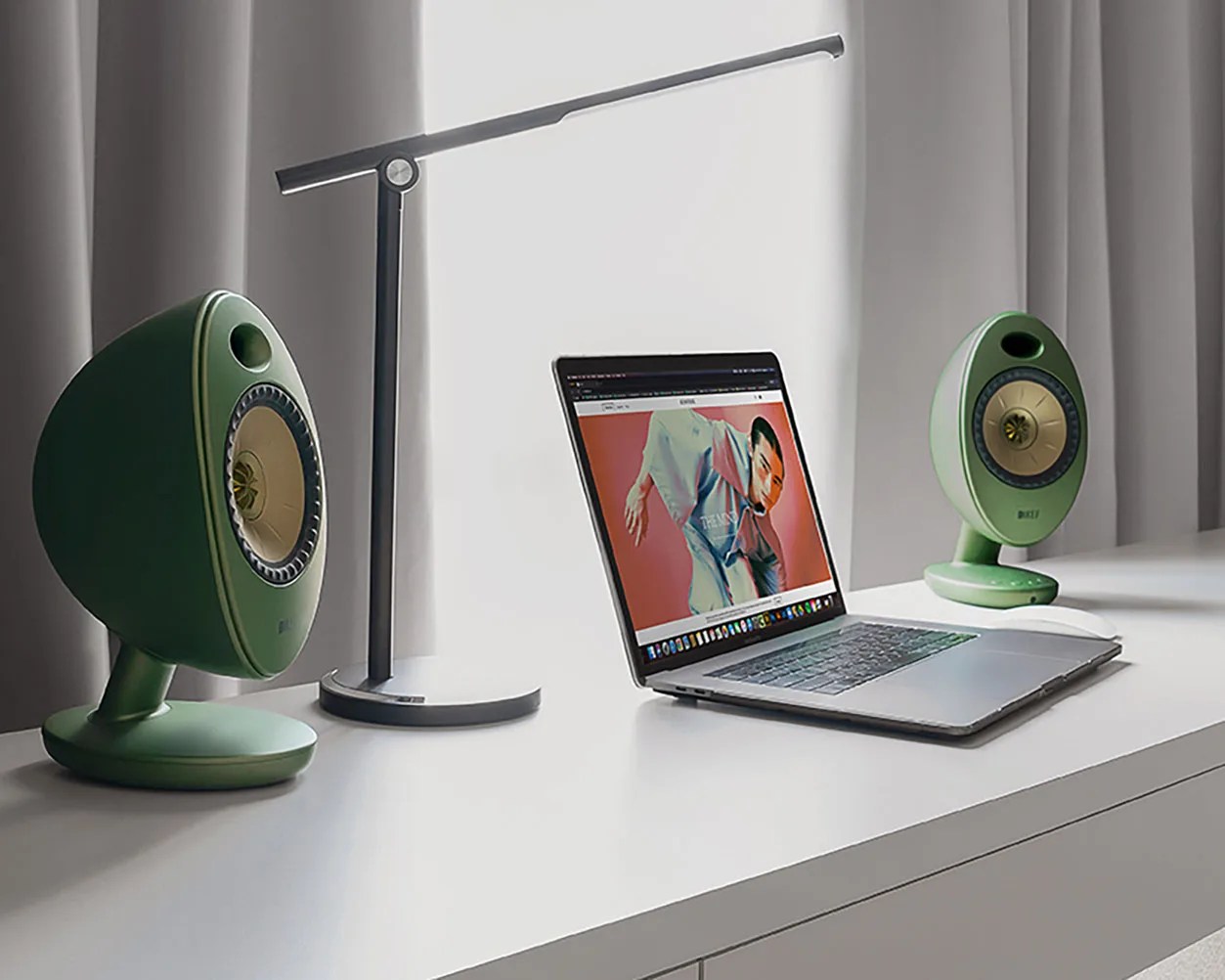 Silver laptop with a colorful screen between two green oval speakers and a black modern desk lamp on a white desk.