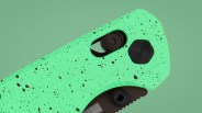 Close-up of a green speckled folding knife handle with black screws and a partially visible blade.