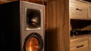 Black Klipsch speaker with copper woofer cone next to a wooden cabinet with drawers.