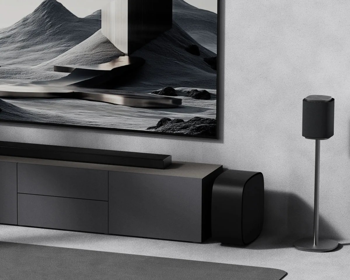 Black soundbar, subwoofer, and speaker on a stand in a modern living room with a large abstract wall art.