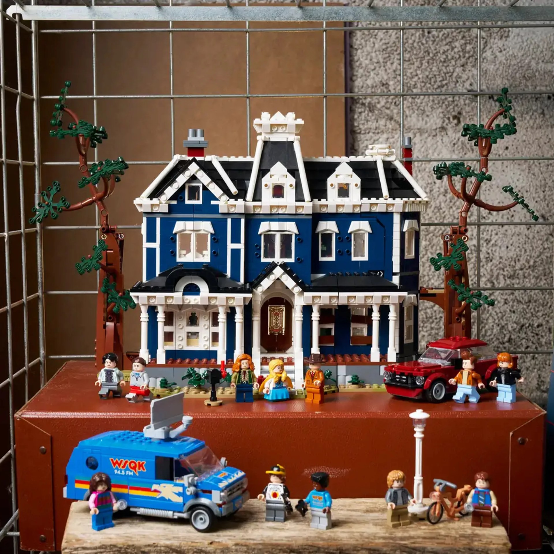 Blue and white LEGO Victorian-style house with trees, a red car, a blue news van, and multiple minifigures.